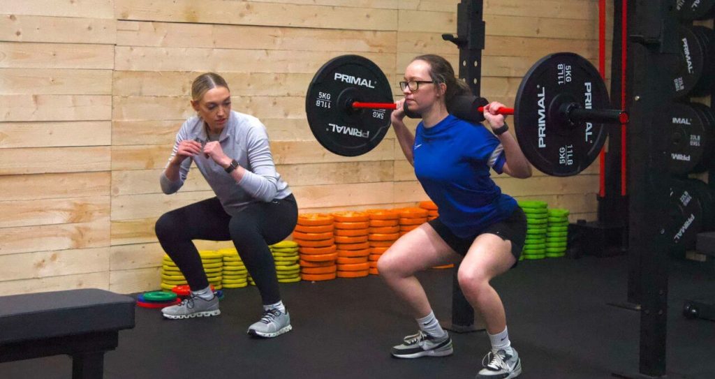 Woman learning correct squat form in a beginner PT session