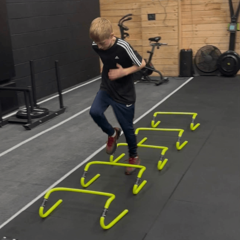 Boy in a gym jumping over a row of small yellow hurdles during an agility drill