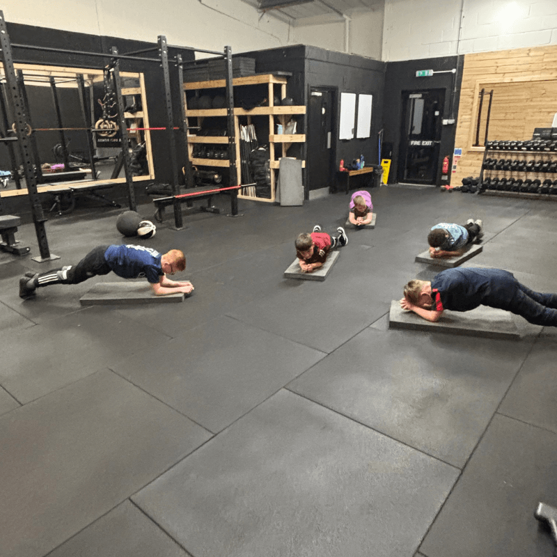 Group of people in a gym performing forearm planks on padded mats during a workout class.